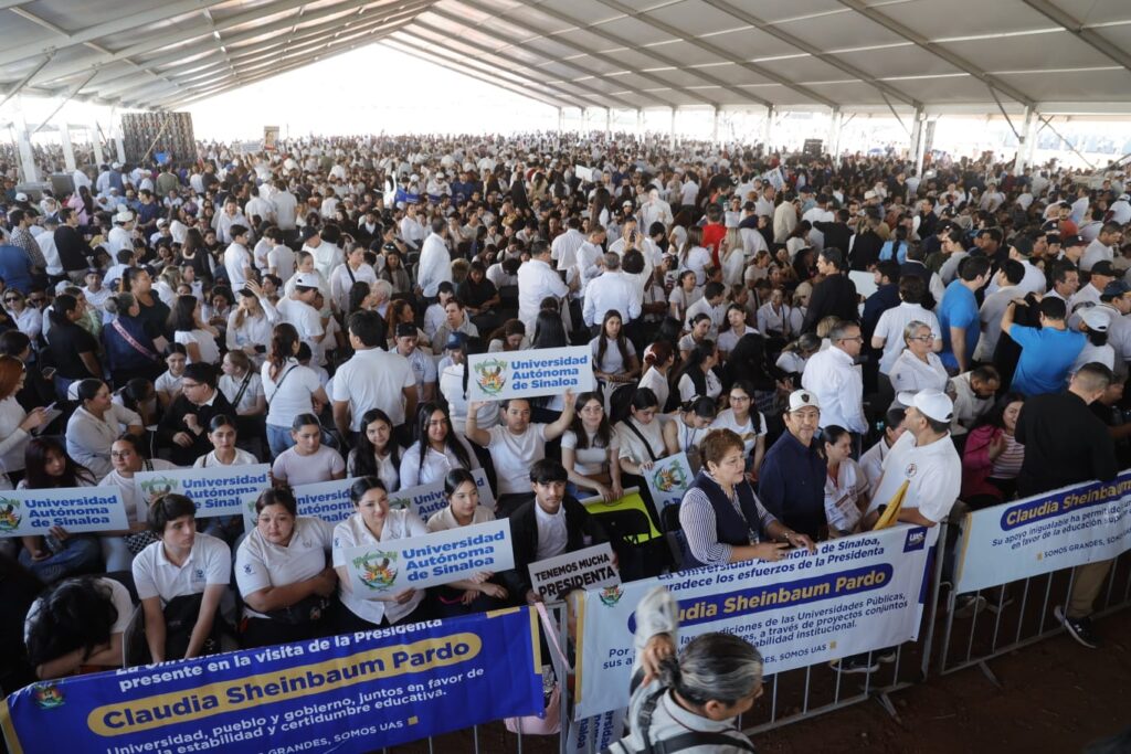 Multitud de personas reunidas bajo una carpa, muchas de ellas vistiendo camisetas blancas, sosteniendo pancartas de la Universidad Autónoma de Sinaloa y mostrando apoyo a Claudia Sheinbaum.